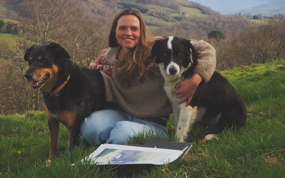 Un femme est assise en montagne en faisant un calin à deux chiens 